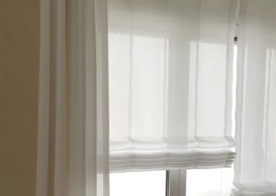 Wohnzimmerfenster mit eleganten Raffrollos in neutralen Farben für stilvolle Lichtregulierung und Gemütlichkeit.